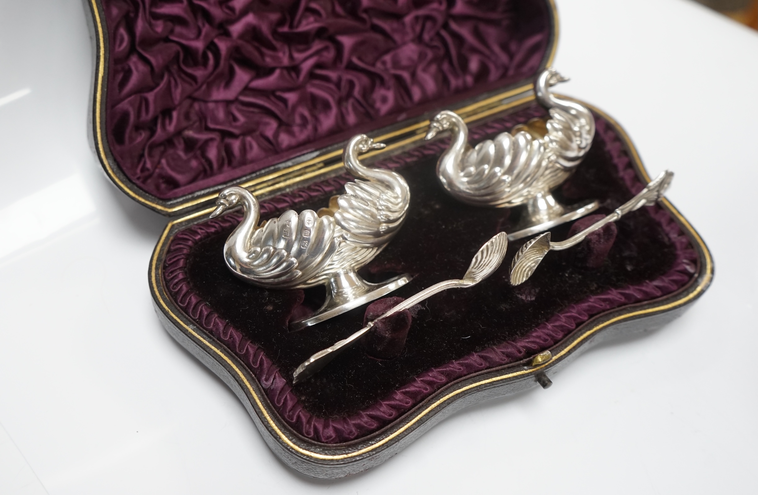 A cased pair of silver double headed swan shaped salts and spoons, Hilliard & Thomasson, Birmingham, 1896, a pair of later silver mounted dwarf candlesticks and a plated butter shell. Condition - fair